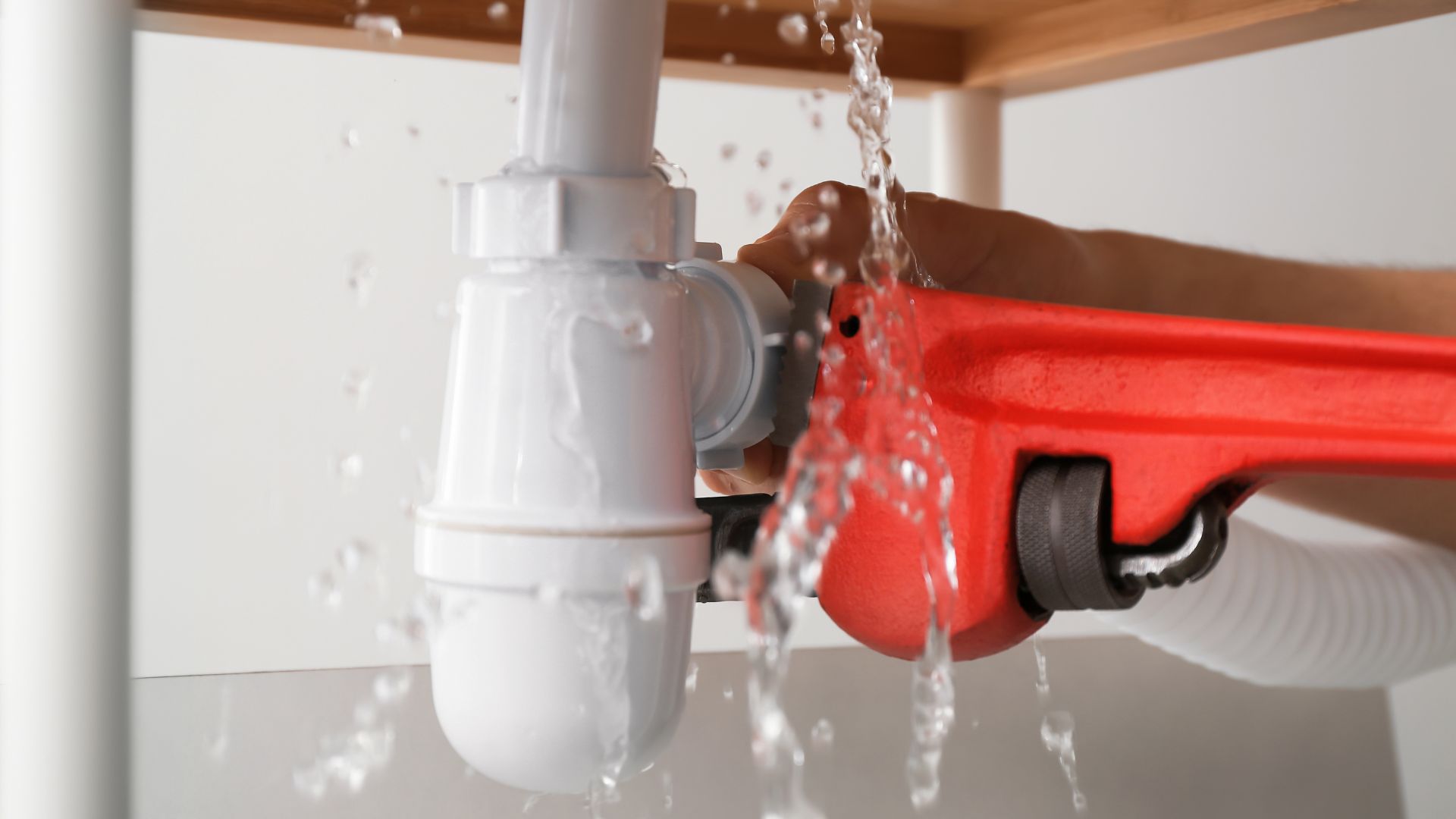 Red pipe wrench fixing leaking plumbing pipe with water spraying