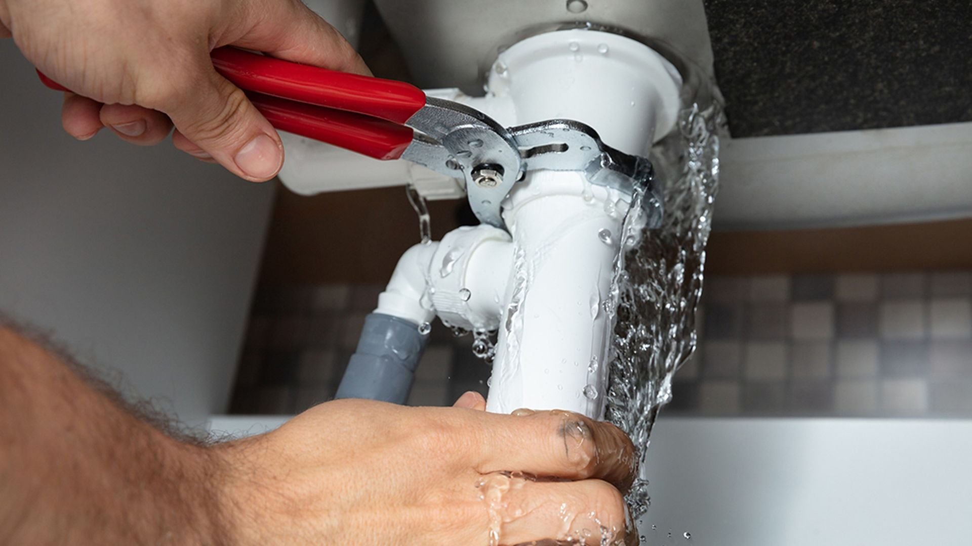 Plumber using red wrench to repair leaking white water pipe